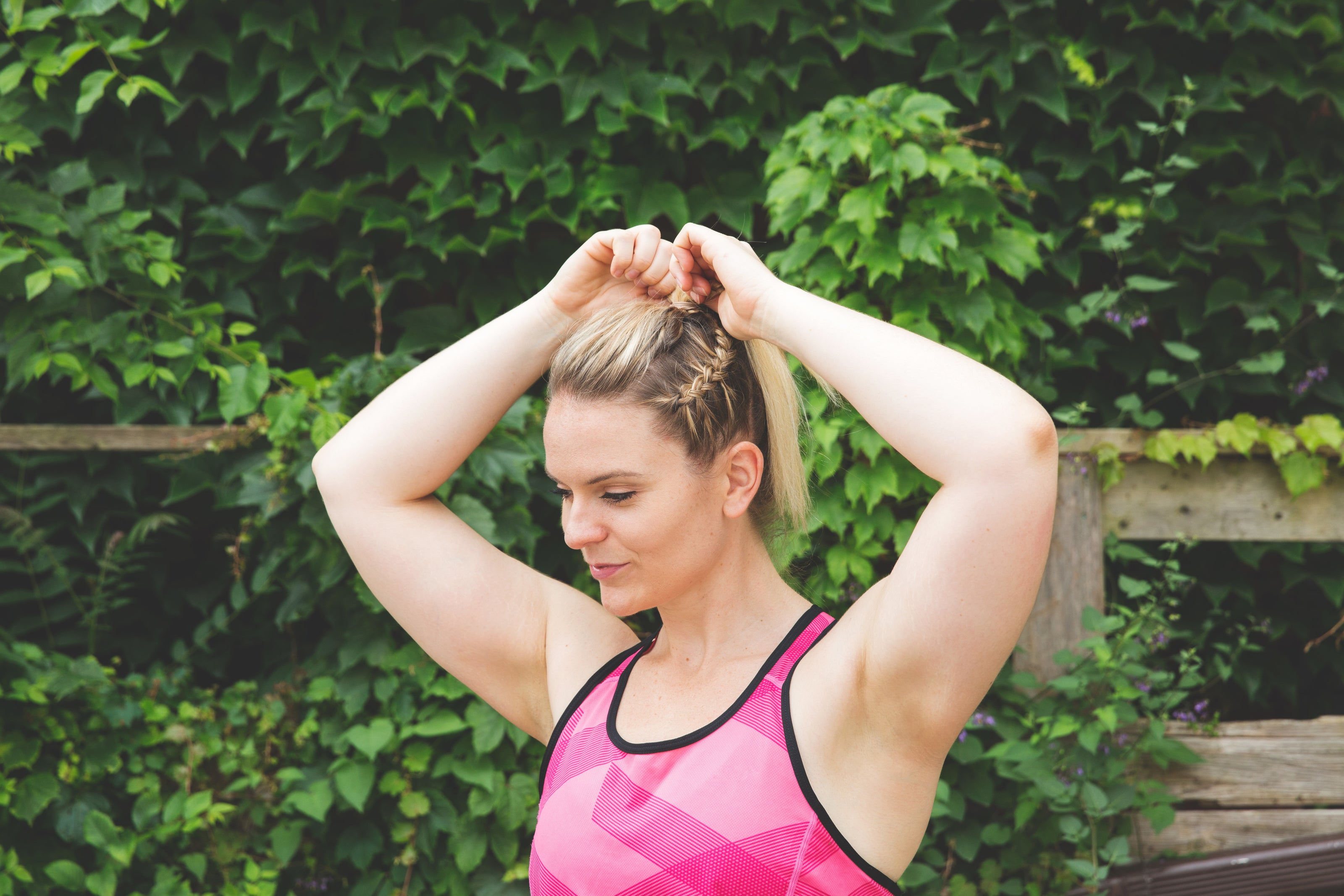 a woman in a pink athletic top putting her hair in ponytail